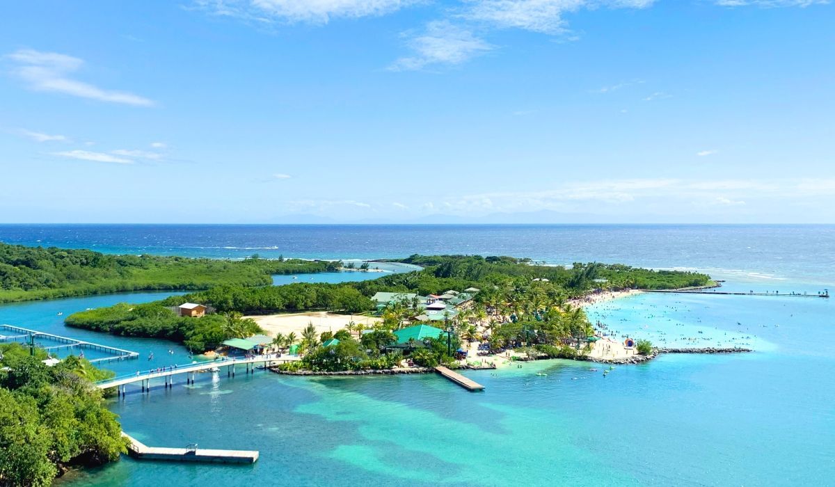 Oceanfront park and beach in Roatán, Honduras with lush greenery and people enjoying the water.