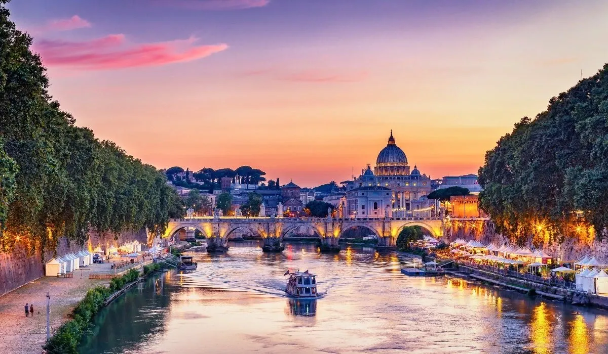 Twilight view of Rome, Italy with St. Peter’s Basilica illuminated above the Tiber River and vibrant city lights reflecting on the water. Canadians purchasing property in Italy can access competitive CAD to EUR rates and seamless transfers with MTFX.