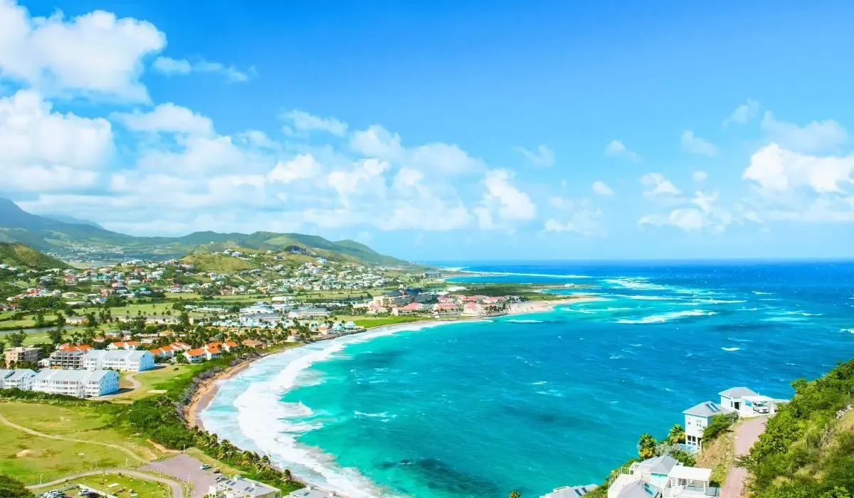 Panoramic view of the coastline in Saint Kitts and Nevis with turquoise waters, rolling green hills, and vibrant coastal homes under a blue sky. Canadians buying property in Saint Kitts and Nevis can benefit from competitive CAD to USD rates and seamless international transfers through MTFX.