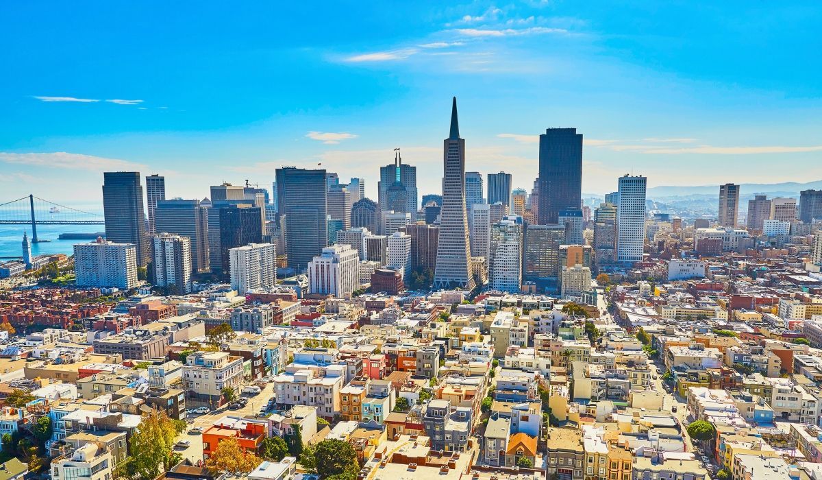 An aerial shot of San Francisco's cityscape, highlighting the Golden Gate Bridge, historic buildings, and surrounding bay waters.​