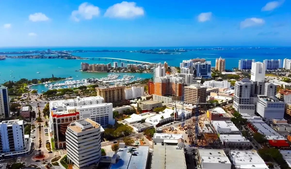 An aerial shot of Sarasota's coastline, showcasing white sandy beaches, turquoise waters, and the iconic Ringling Bridge connecting the city to barrier islands.