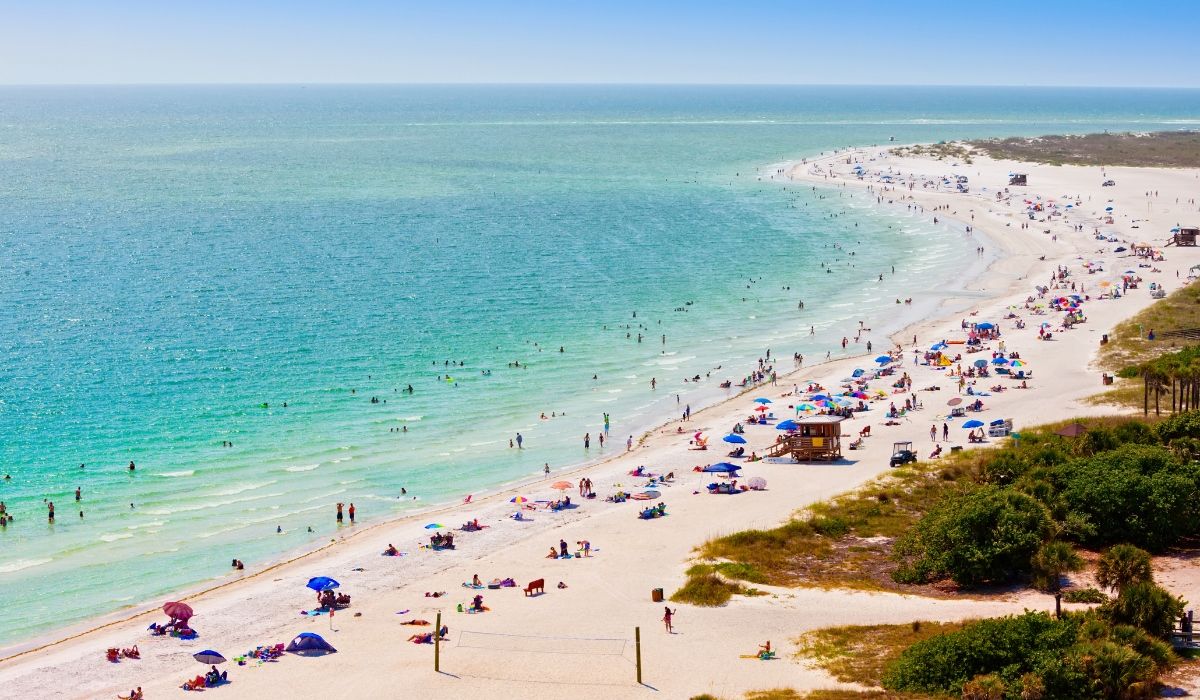 A coastal view of Sarasota, Florida, showcasing white sandy beaches, turquoise waters, and luxury condominiums along the shoreline.