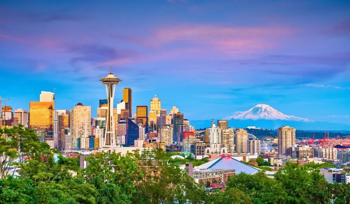An aerial view of Seattle's iconic skyline showcasing the Space Needle, modern skyscrapers, and Mount Rainier visible in the distance under a sunny sky.