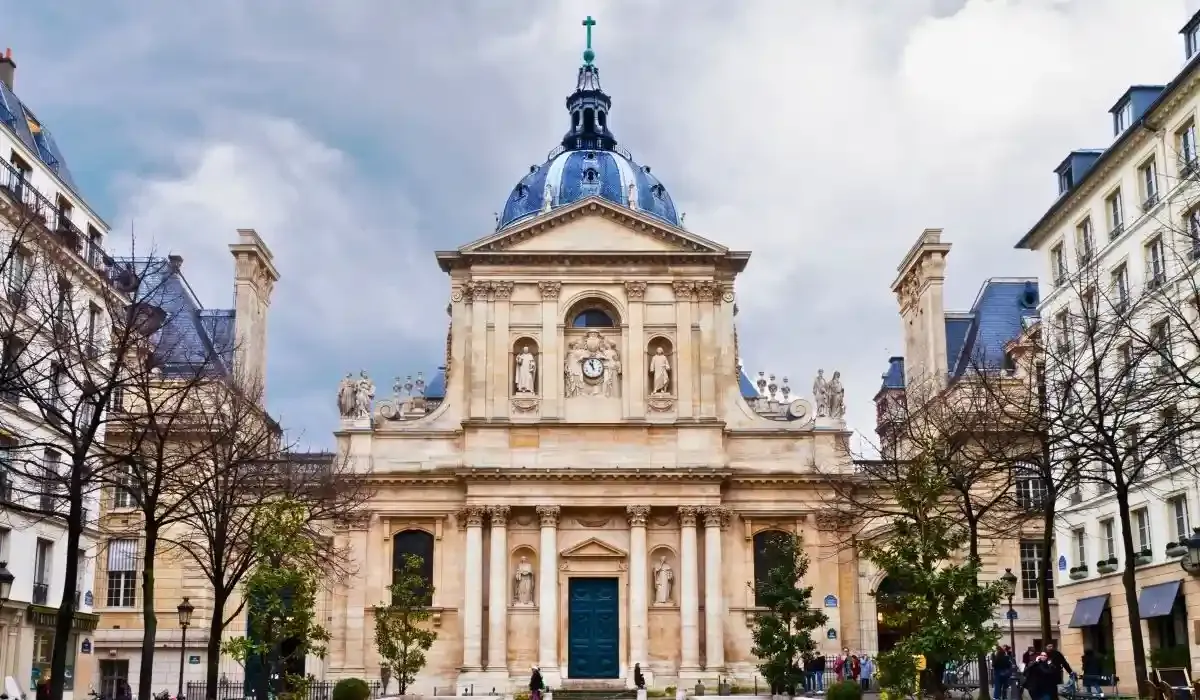 Classical facade of Sorbonne University in Paris with its iconic dome and historic statues under a cloudy sky.