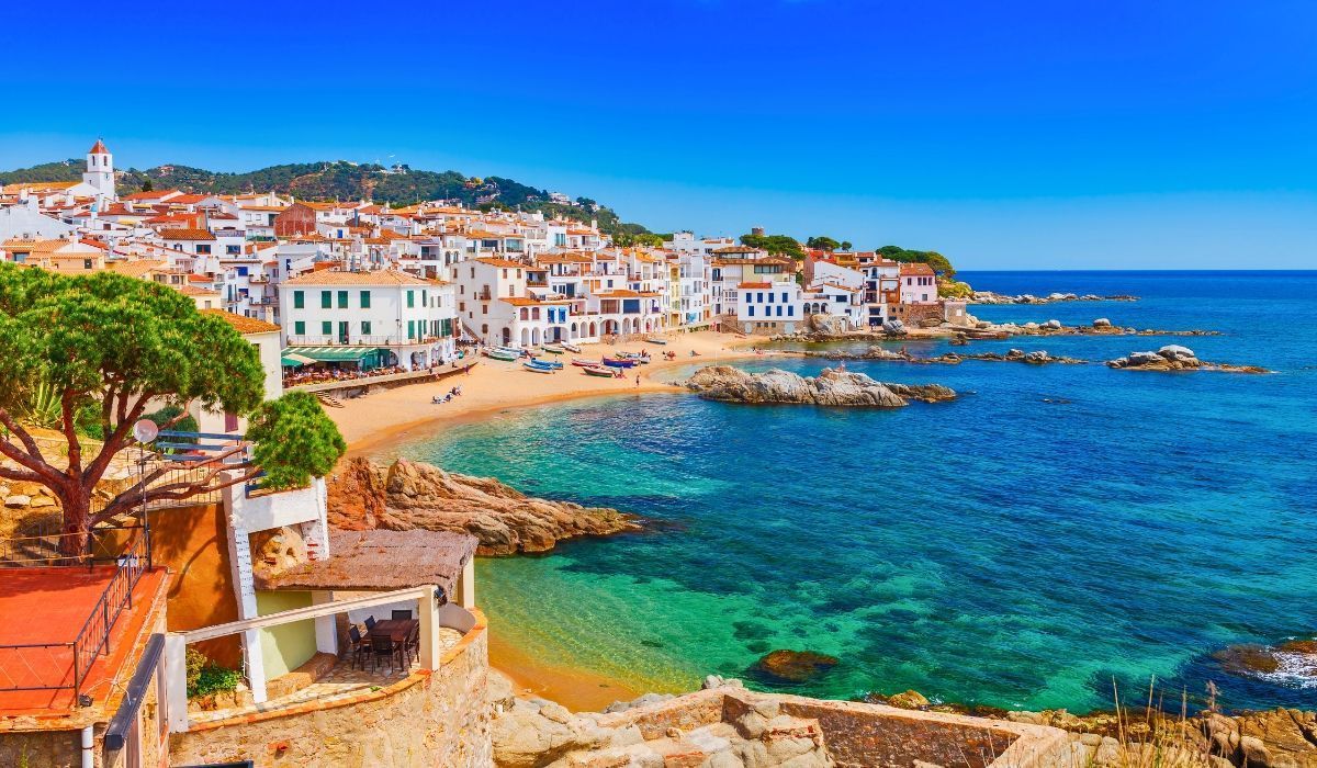 Scenic view of a coastal town in Spain with colorful houses and a calm blue sea, ideal for Canadians investing in European real estate.