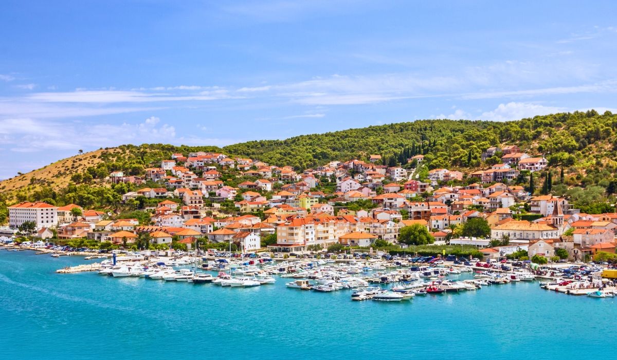 A scenic coastal town with terracotta-roofed buildings and a packed marina full of boats.