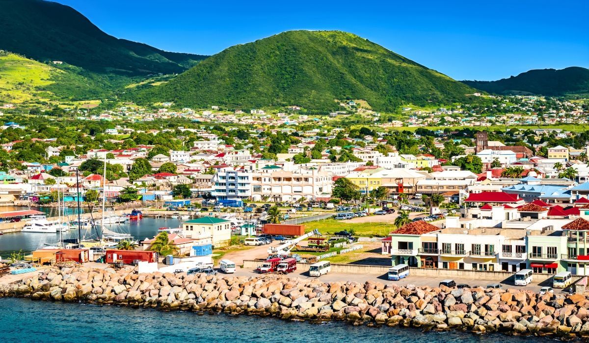 Coastal view of Basseterre, St. Kitts with buildings lining the shore and lush green hills in the background.