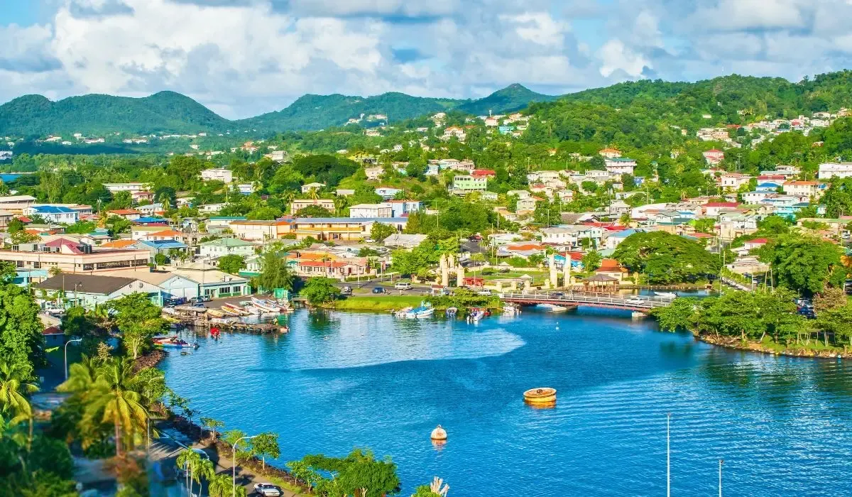 A panoramic view of St. Lucia's iconic Pitons rising above lush greenery, with turquoise waters and a serene beach in the foreground.
