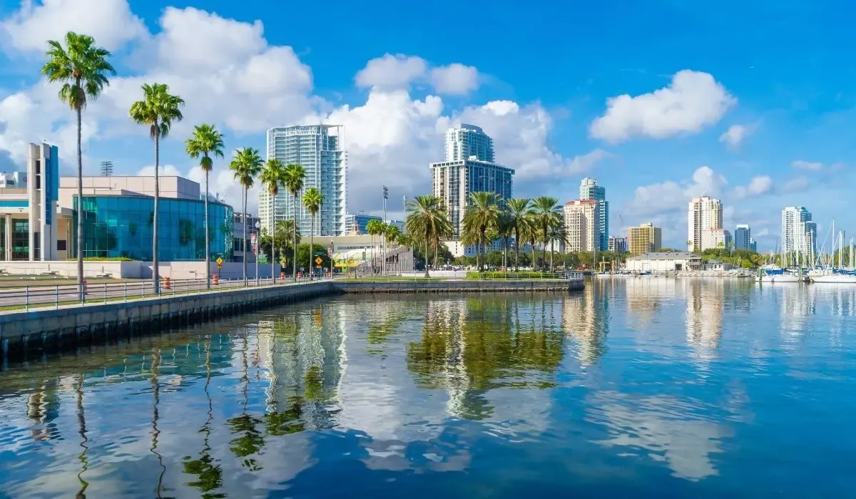A scenic view of St. Petersburg's waterfront, featuring a marina filled with boats, palm-lined promenades, and a vibrant downtown skyline under a clear blue sky.