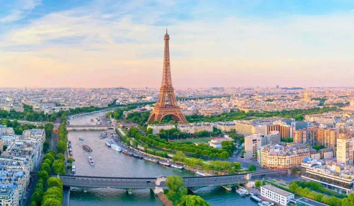 A scenic view of the Eiffel Tower and the Seine River in Paris, France, surrounded by lush greenery and city architecture during a sunny day.