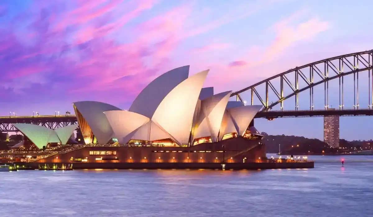 A twilight view of the Sydney Opera House and Harbour Bridge illuminated along the waterfront.