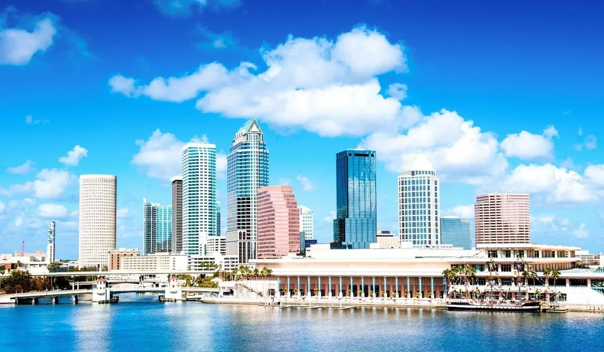 Modern skyline of downtown Tampa, Florida, with tall buildings reflecting off the calm bay under a bright blue sky.