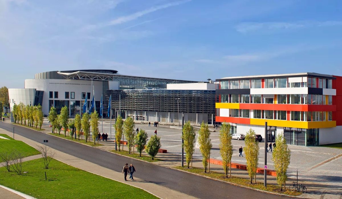 A modern campus view of the Technical University of Munich, with colorful academic buildings, sleek glass architecture, and students walking through the open plaza.