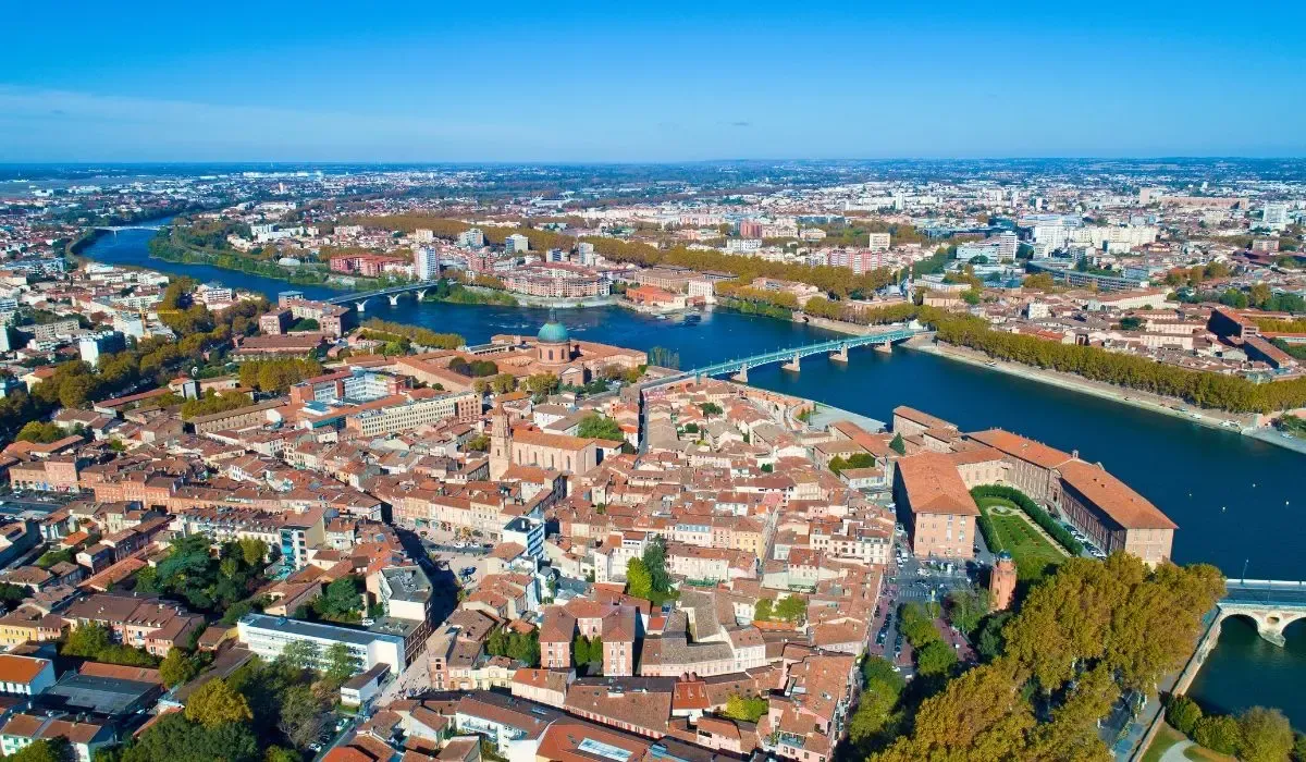 Aerial view of Toulouse, France with red-roofed buildings lining the Garonne River under a bright blue sky. Canadians buying property in France can take advantage of excellent CAD to EUR rates and cost-efficient money transfers with MTFX.