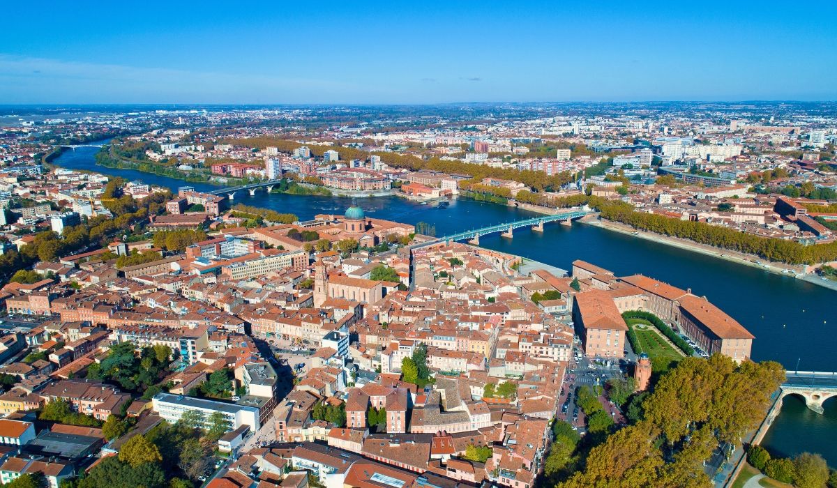 A scenic view of Toulouse's city center with the Garonne River in the foreground and the iconic dome of La Grave hospital in the background.