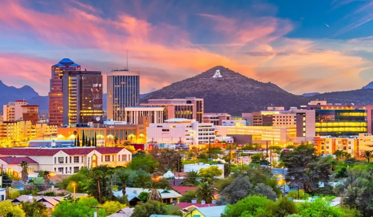 A desert landscape of Tucson, Arizona, featuring saguaro cacti, rugged mountains, and a sunset casting warm hues over the terrain.