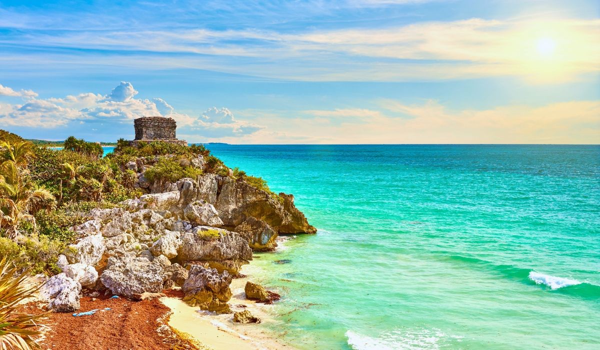 An aerial shot of Tulum's coastline, featuring ancient Mayan ruins perched on cliffs overlooking the Caribbean Sea with pristine beaches below.