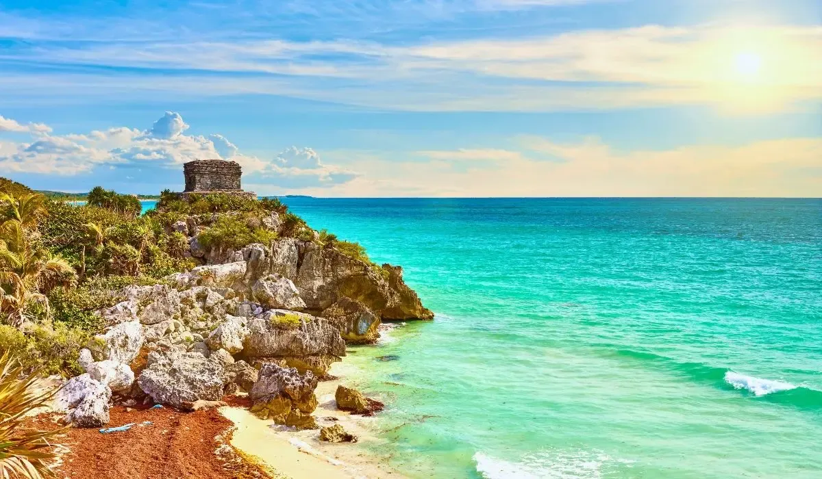An aerial shot of Tulum's coastline, featuring ancient Mayan ruins perched on cliffs overlooking the Caribbean Sea with pristine beaches below.