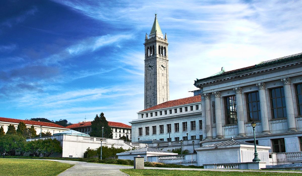 Sather Tower rising above UC Berkeley’s classical architecture, with wide grassy spaces and a dynamic blue sky filled with swirling clouds.