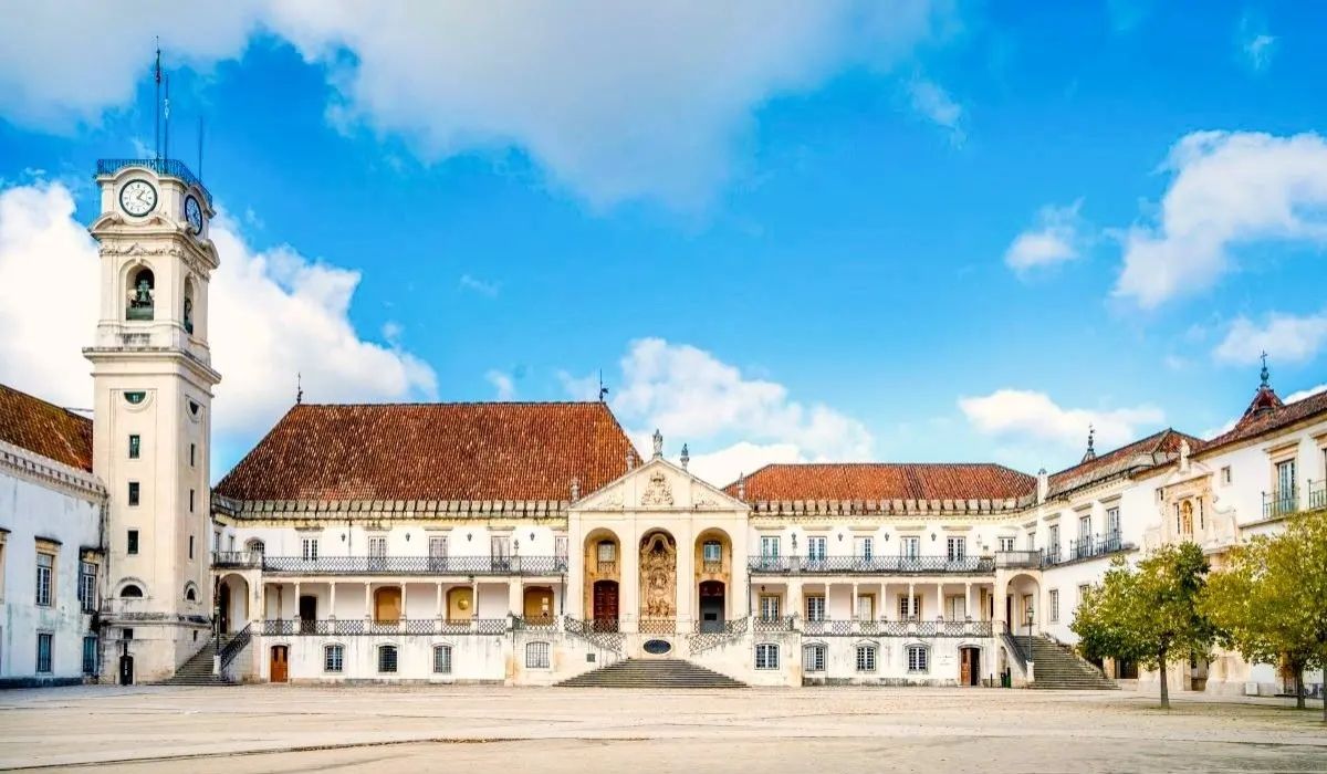 A scenic view of Universidade de Coimbra, displaying historic buildings with ornate details and a central courtyard bustling with students.