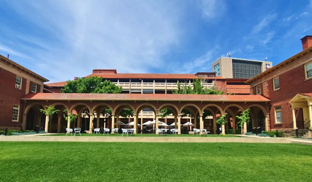 A panoramic view of the University of Adelaide campus, featuring historic sandstone buildings surrounded by lush greenery under a clear blue sky.