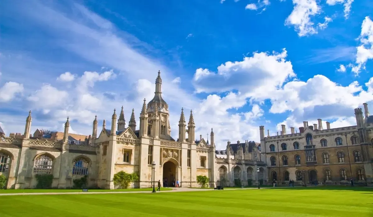 The iconic King's College Chapel at the University of Cambridge, set against a blue sky with manicured lawns and Gothic-style architecture.