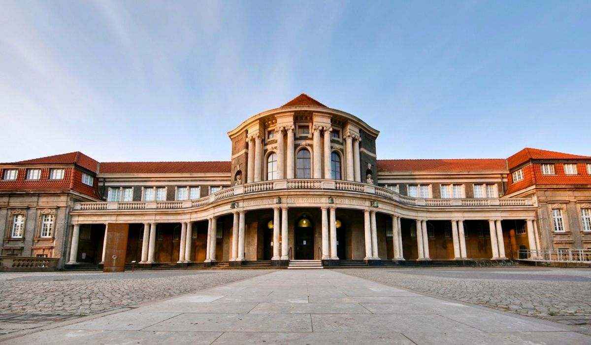 Front view of the University of Hamburg’s main building, featuring a neoclassical façade with a columned portico and a red-tiled roof under a clear sky.