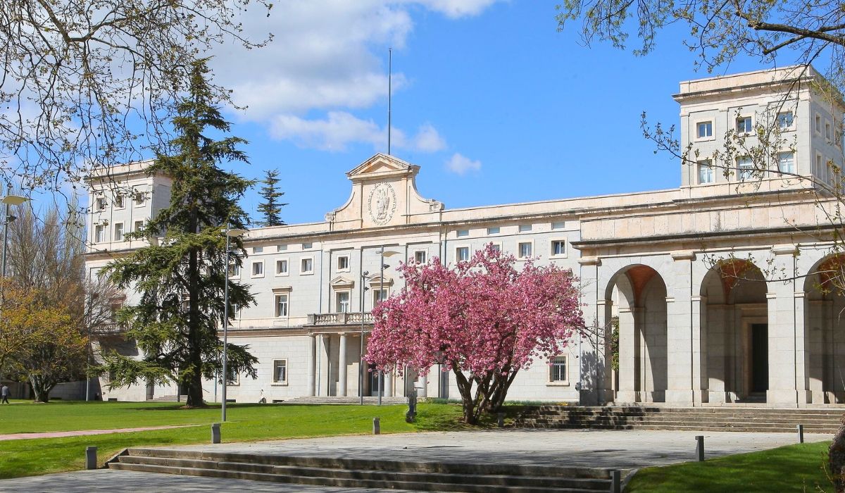 Neoclassical campus building of the University of Navarra in Spain, with blooming cherry blossom trees and manicured lawns.