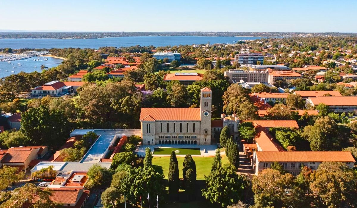 Aerial view of the University of Western Australia’s scenic riverside campus with red-roofed buildings surrounded by trees.