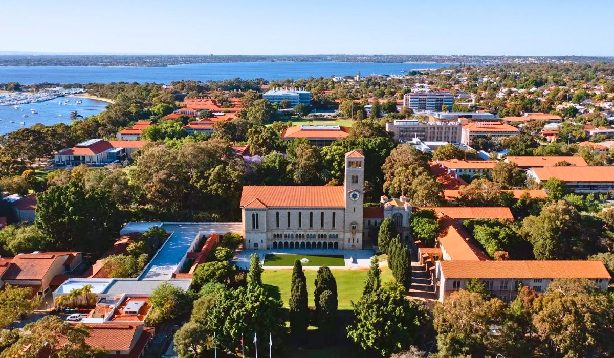 A scenic image of the University of Western Australia, featuring the iconic Winthrop Hall with its Romanesque architecture and adjacent reflection pool.​