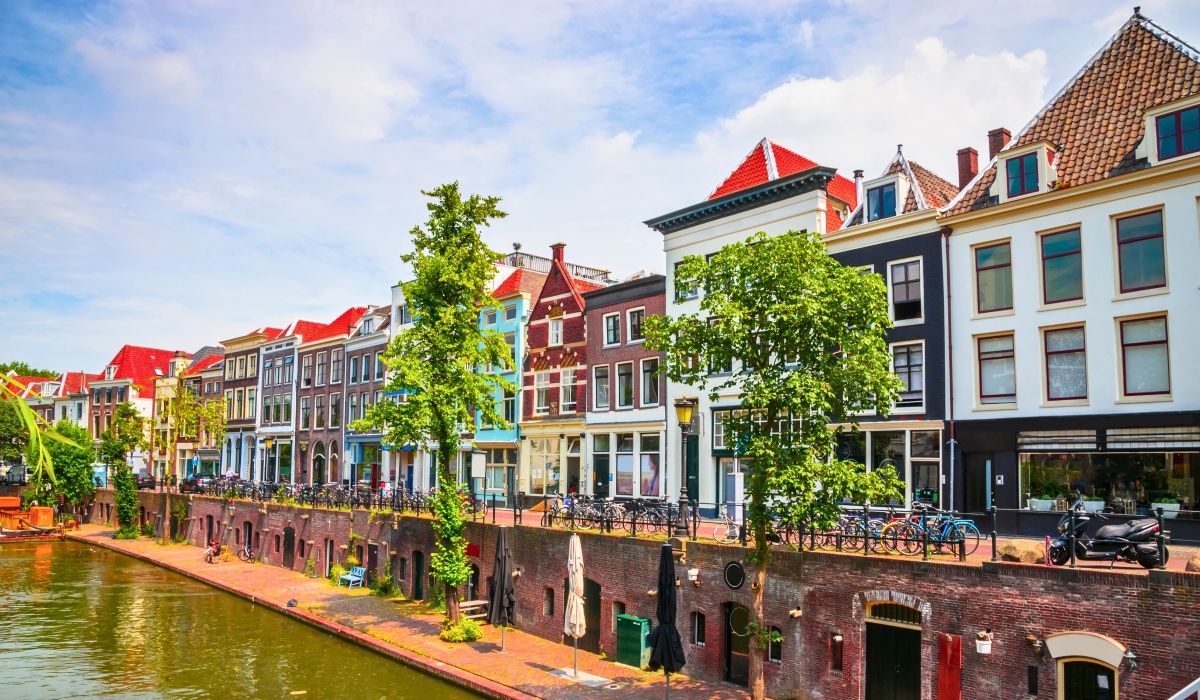 Charming canal scene in Utrecht, lined with colorful historic houses, trees, and bicycles along the water's edge.