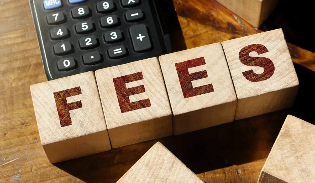 Wooden blocks spelling fees beside a calculator on a desk representing currency conversion costs, bank charges, and hidden transfer fees.