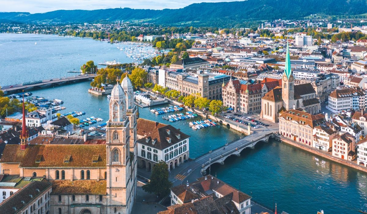 Aerial view of Zurich, Switzerland, showcasing historic churches, riverside buildings, and boats docked along Lake Zurich.