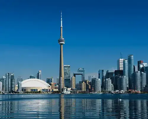 Toronto skyline featuring the CN Tower and modern city buildings reflected in the water under a clear blue sky.