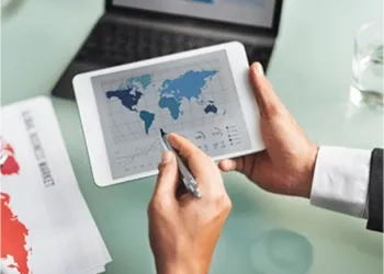 Hand holding a tablet displaying a world map with financial data charts