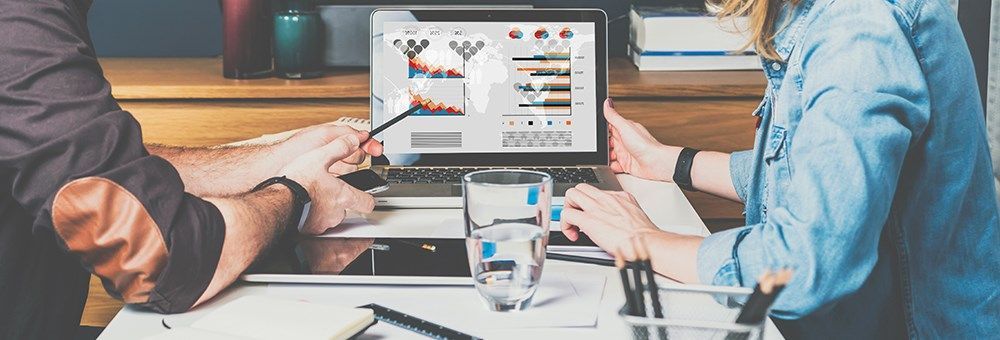 Two people analyzing financial data on a laptop screen, which displays colorful charts and graphs, representing foreign exchange trends and market insights.