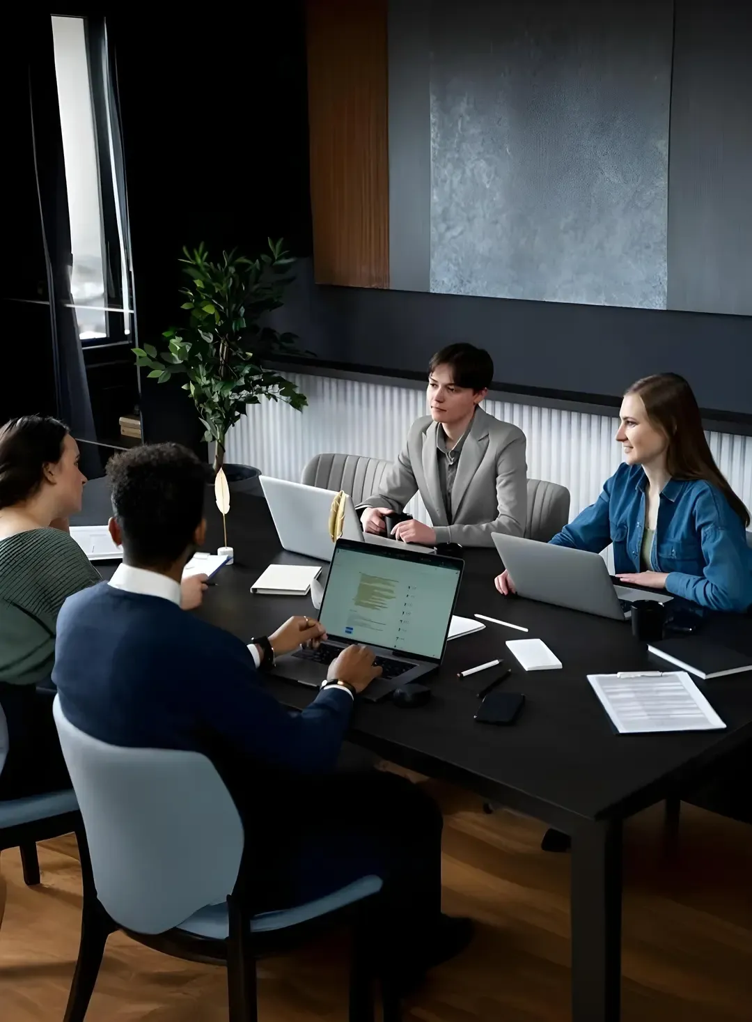 Group of coworkers collaborating around a conference table with laptops and documents