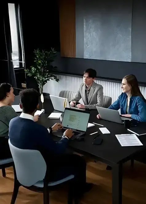 Group of coworkers collaborating around a conference table with laptops and documents