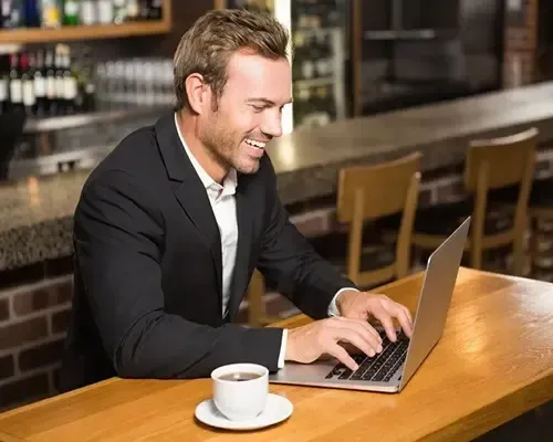 Smiling businessman working on a laptop at a coffee shop counter with a cup of coffee in front of him