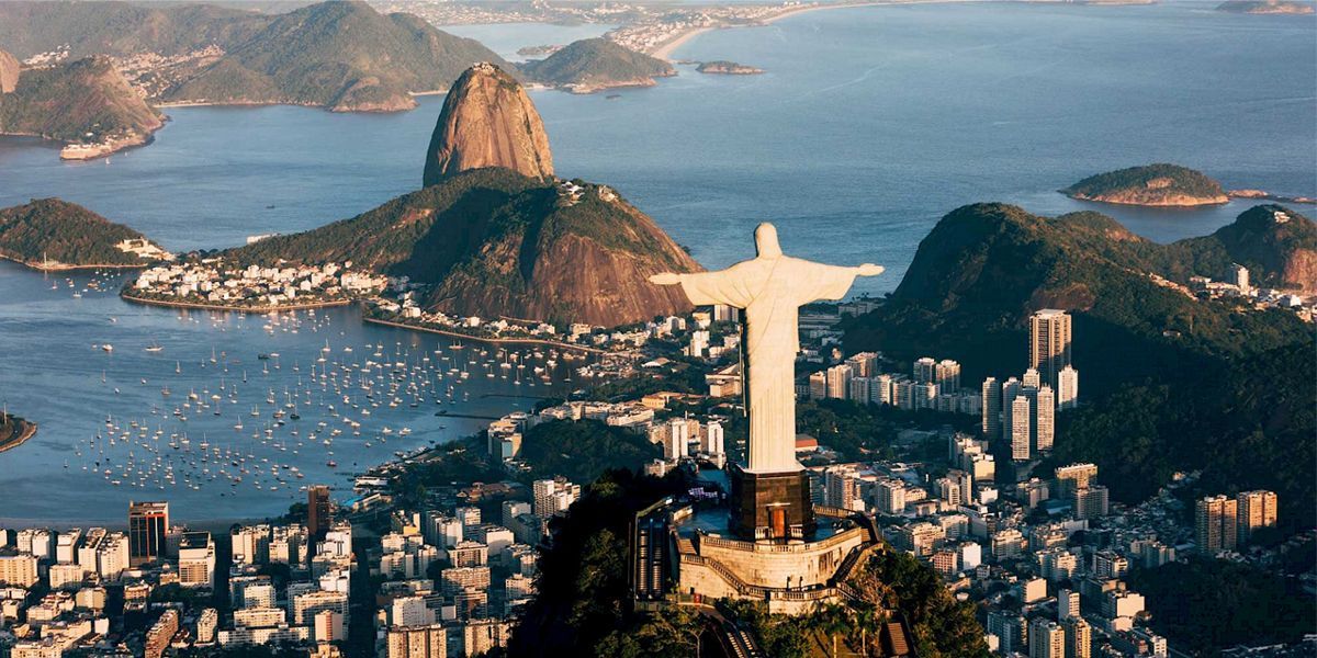 Aerial view of Rio de Janeiro, Brazil, featuring the Christ the Redeemer statue overlooking the city, Sugarloaf Mountain, Guanabara Bay, and surrounding coastal landscape.