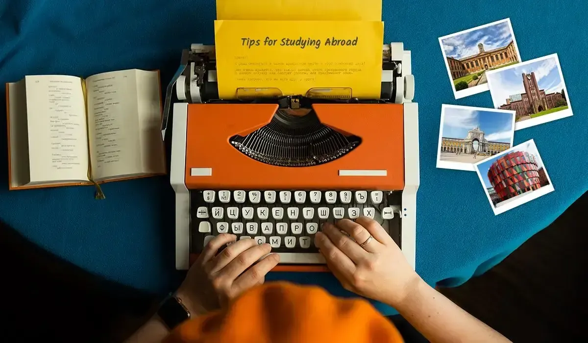 An image of hands typing on an orange typewriter with a paper reading 'Tips for Studying Abroad,' surrounded by a book and travel postcards on a blue tablecloth.