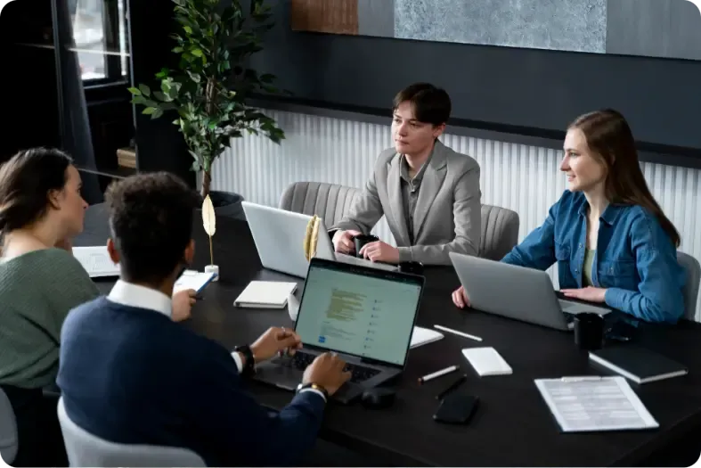 Team of professionals collaborating around a conference table with laptops and documents during a business meeting in a modern office setting.