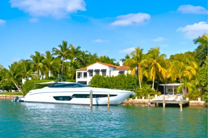 Luxury waterfront mansion with a private dock and yacht surrounded by palm trees