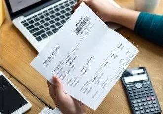 Person reviewing a utility or tuition bill next to a laptop and calculator, preparing for an international payment.