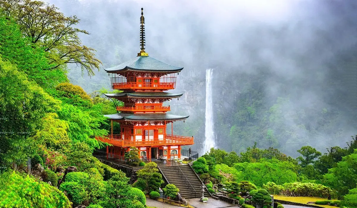A scenic view of a traditional Japanese pagoda surrounded by lush greenery and a cascading waterfall.