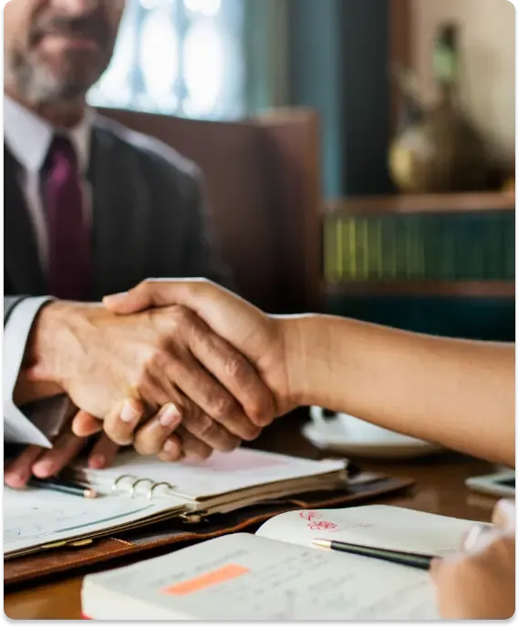 Close-up of a handshake between two people over legal documents, symbolizing agreement or transfer of inheritance funds.