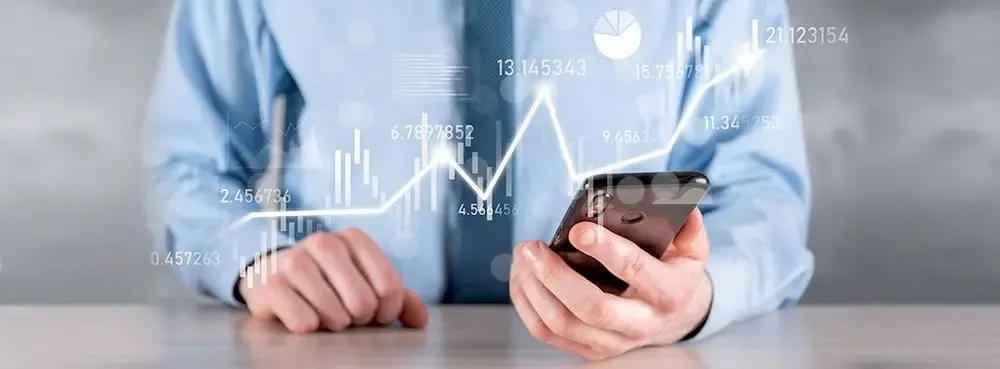 Businessman analyzing financial data on smartphone with digital graphs and currency figures overlayed, symbolizing savings on overseas money transfers.