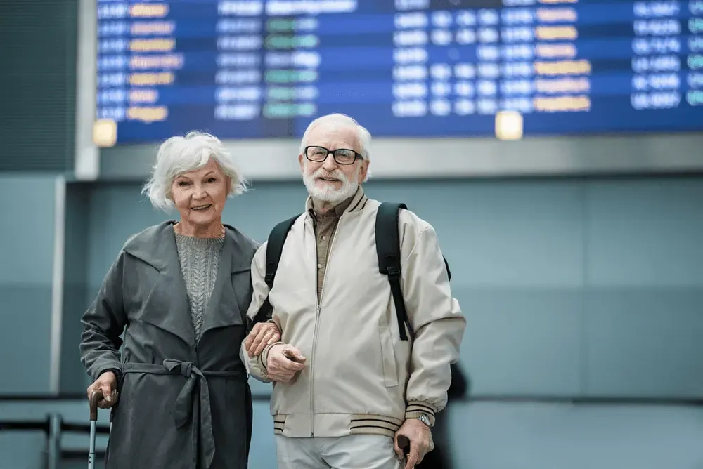 Smiling senior couple at an airport terminal with luggage, preparing to retire abroad and begin their international journey.