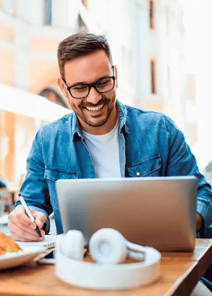 Smiling man managing regular international transfers on his laptop at an outdoor café.