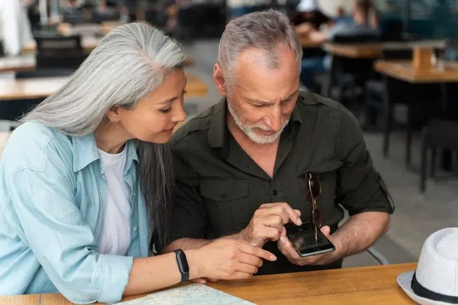 Older couple sitting at a cafe table looking at a smartphone together